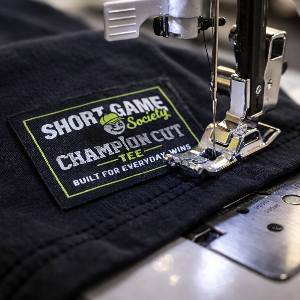 Embroidery machine stitching a label onto a black fabric with 'Short Game Society' branding.