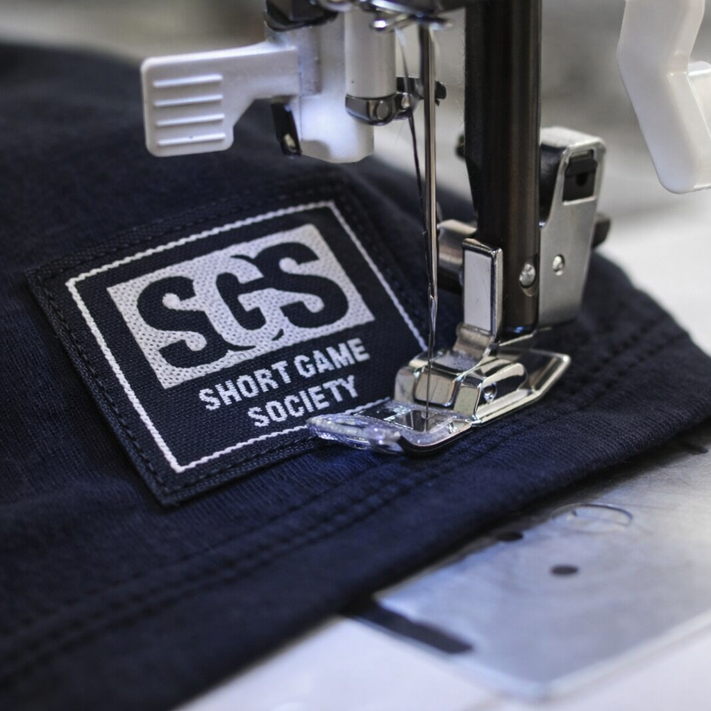 Embroidery machine stitching a 'Short Game Society' patch onto a piece of fabric.